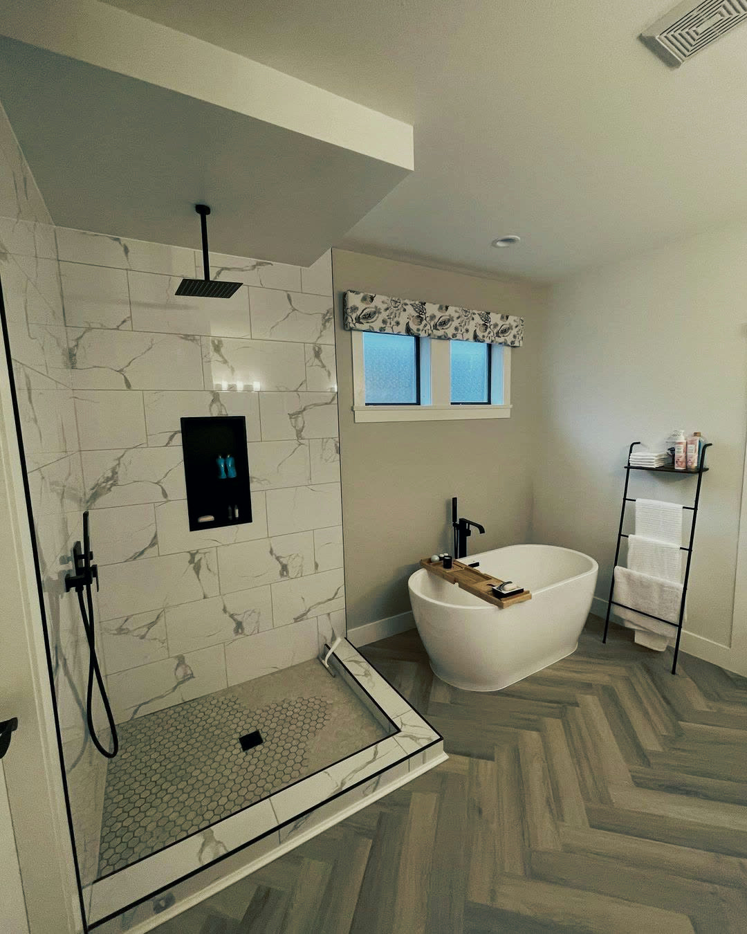 Completed walk-in shower with marble-look tile, a black rain head, recessed niche and hex mosaic floor.