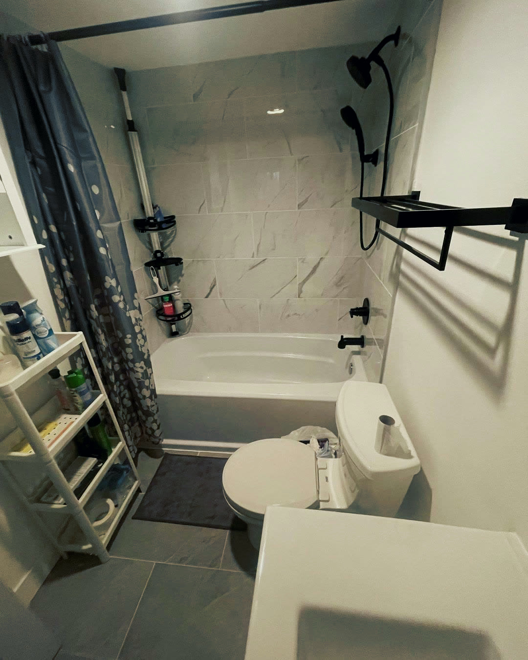 The same bathroom rebuilt with large marble-look tile around the tub and matte black fixtures.