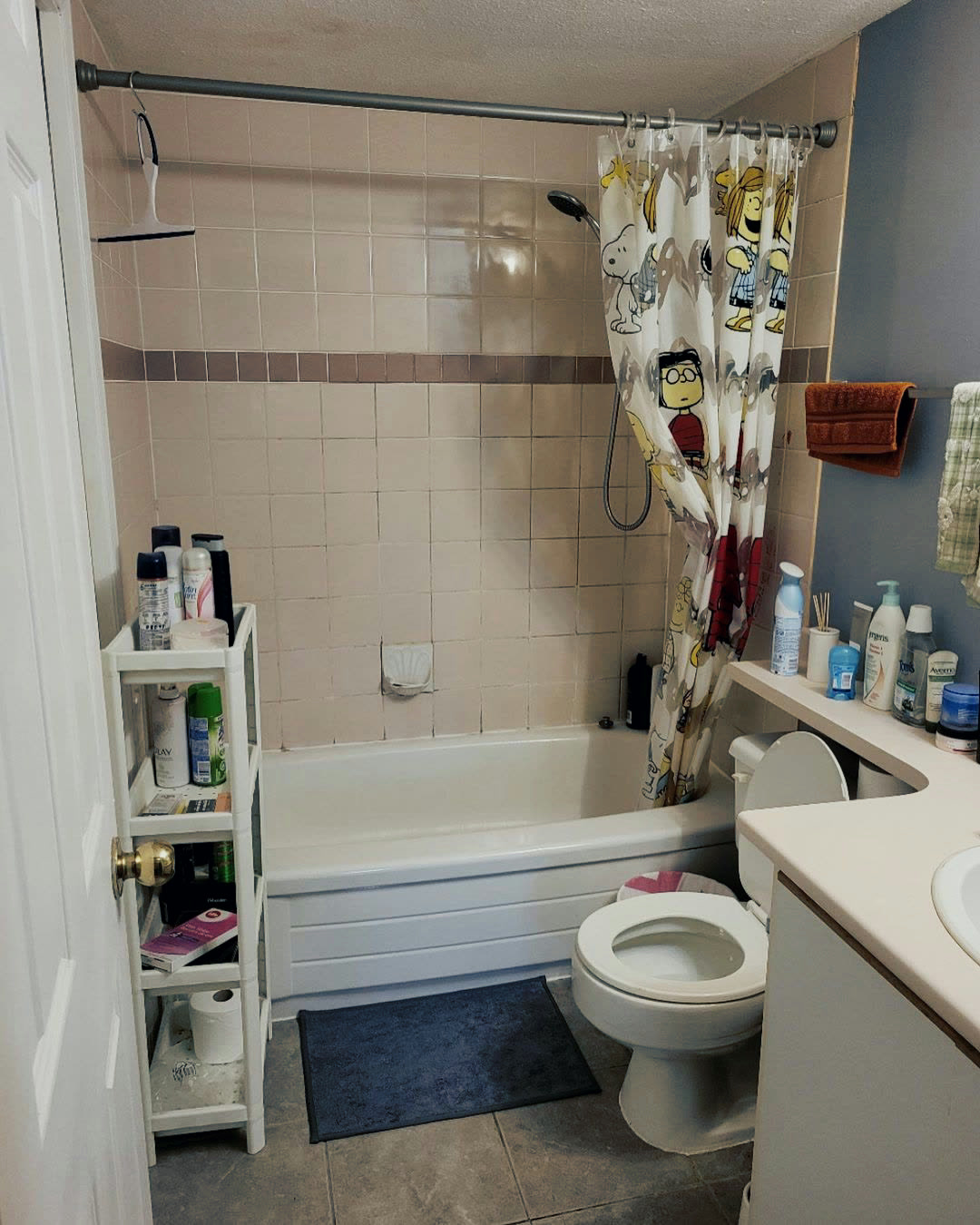 A dated bathroom with pink square wall tile, a bordered tile band and an older vanity.
