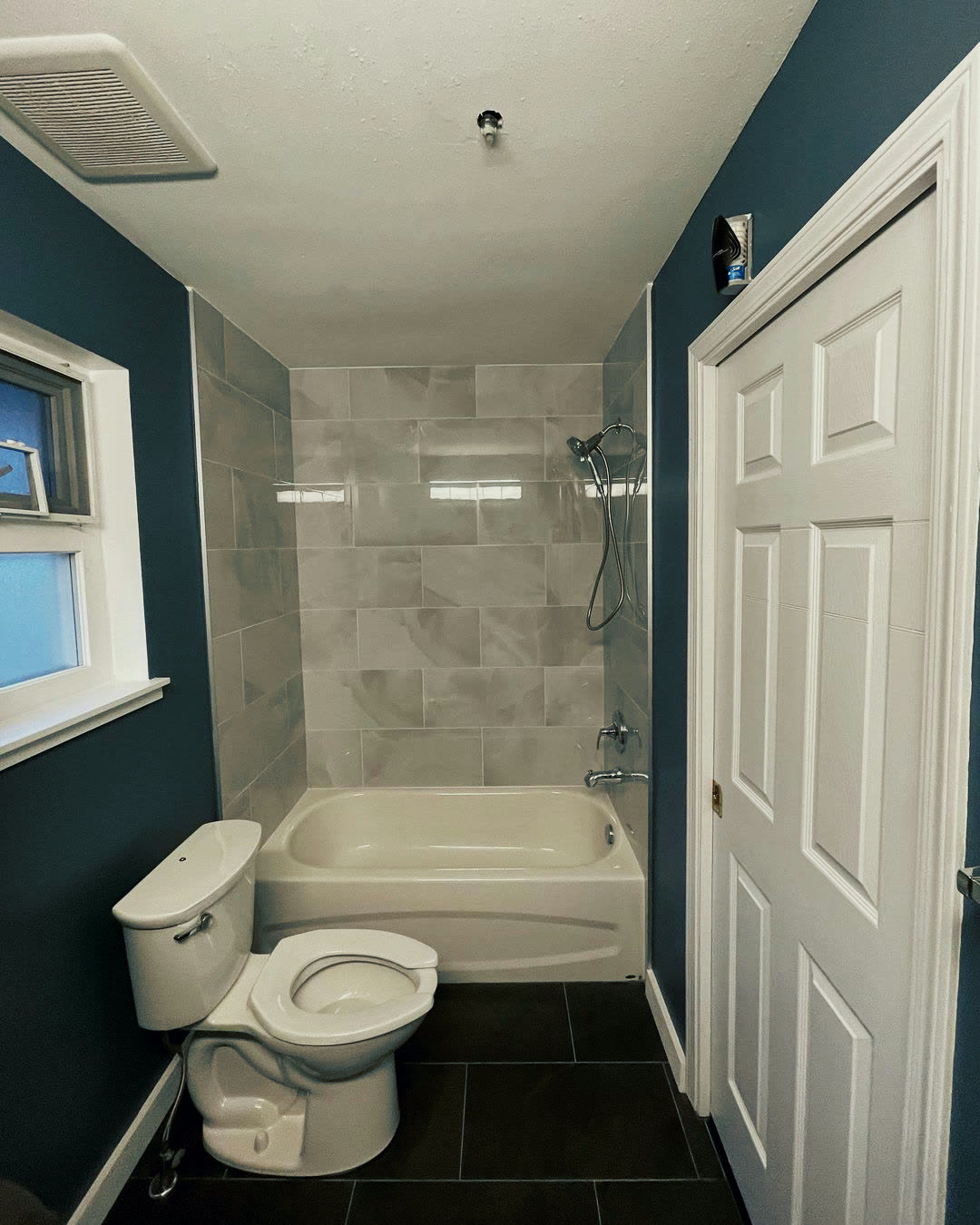 The finished bathroom in deep teal, with a tiled tub surround, recessed niche and dark slate-look floor.