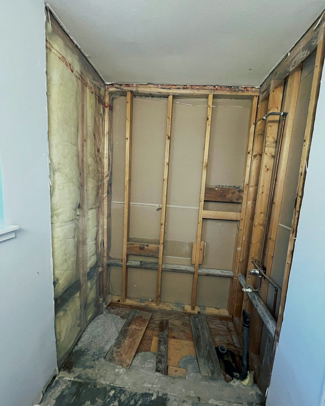 The tub alcove stripped back to studs, with insulation and the shower riser exposed.