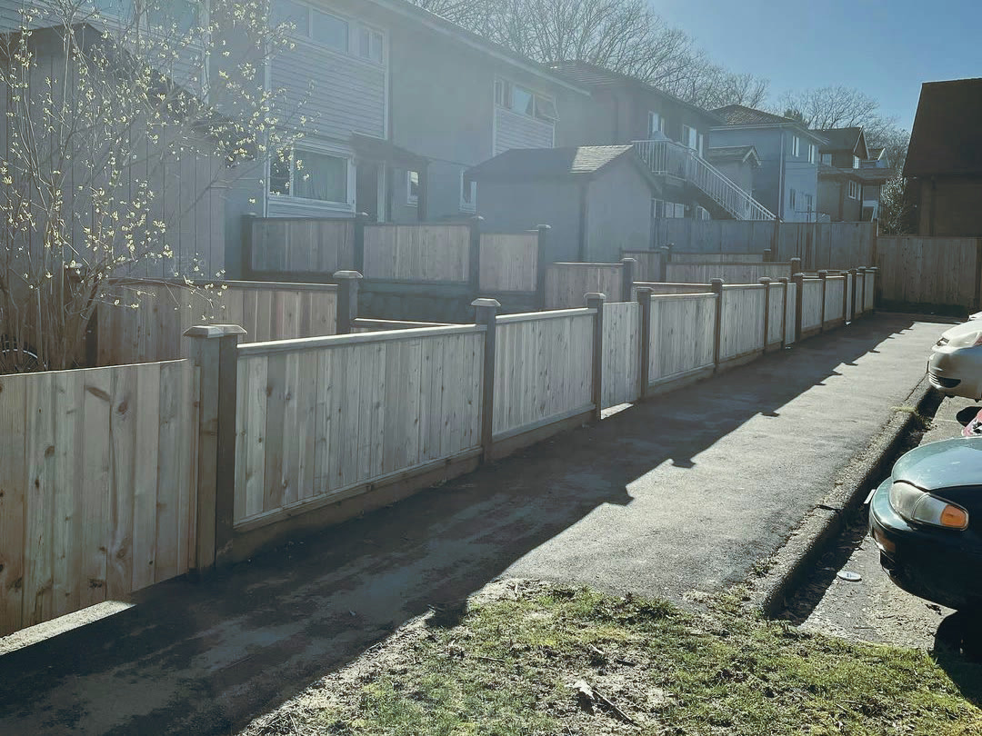 The completed fence stepping down the slope in bays along the parking lane, meeting the older fencing on the level above it.