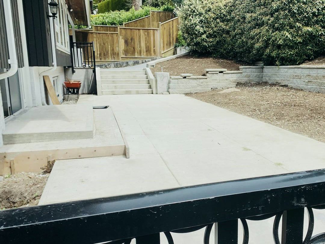 The poured concrete patio running between the house and the new stairs, with formwork still in place along the near edge.
