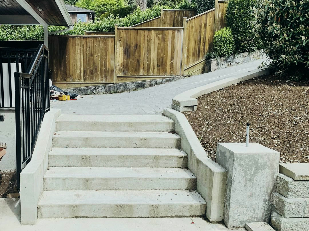 Completed concrete stairs with cast cheek walls, leading to a curved paver walkway edged in concrete.