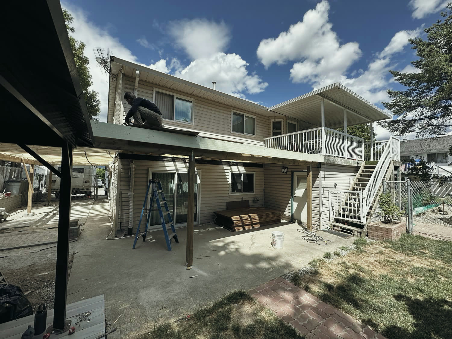 Rear elevation before the new work, showing beige siding, the old white stair and the covered patio below.