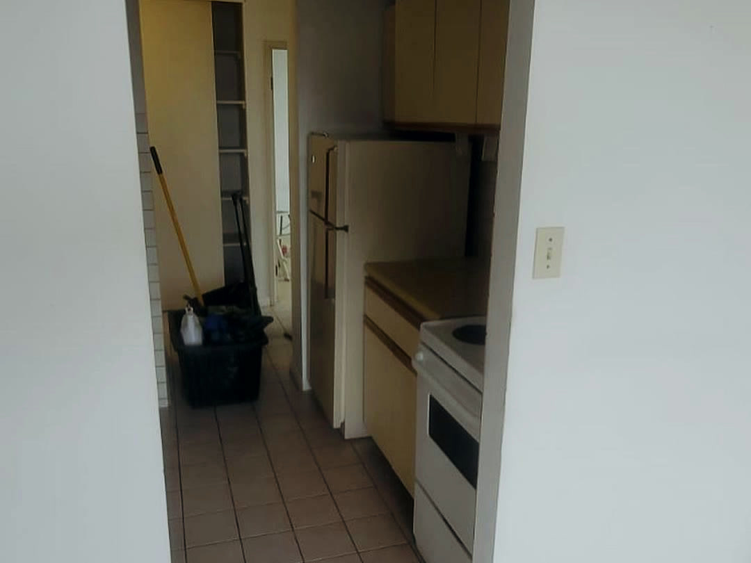 The original galley kitchen behind a partition wall, with almond laminate cabinets, an older range and refrigerator, and brown floor tile.