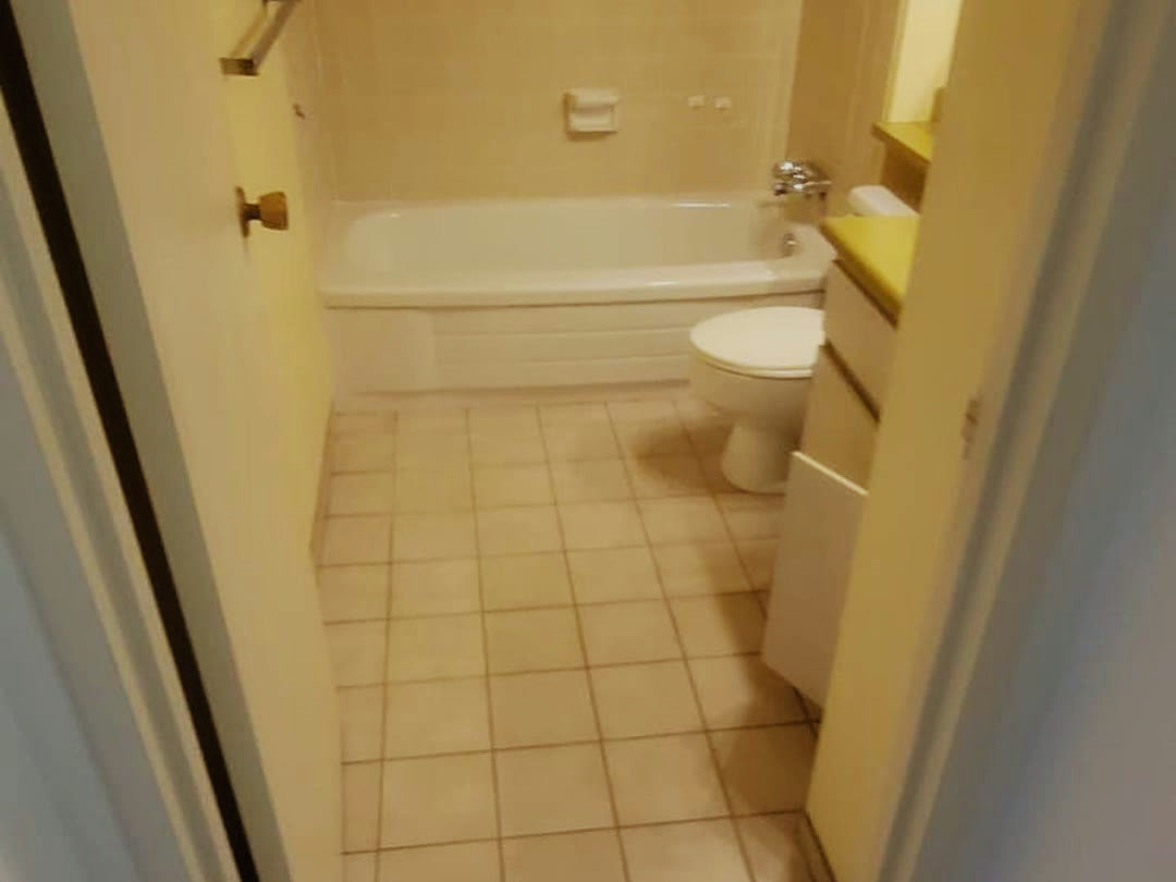 The original bathroom, tiled floor to ceiling in beige, with a dated vanity and tub.