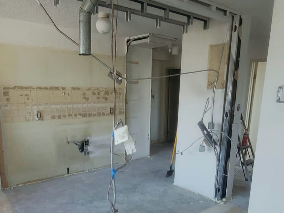 The kitchen stripped back — wall tile removed to the substrate, plumbing and electrical left exposed, and a doorway reframed in steel stud.
