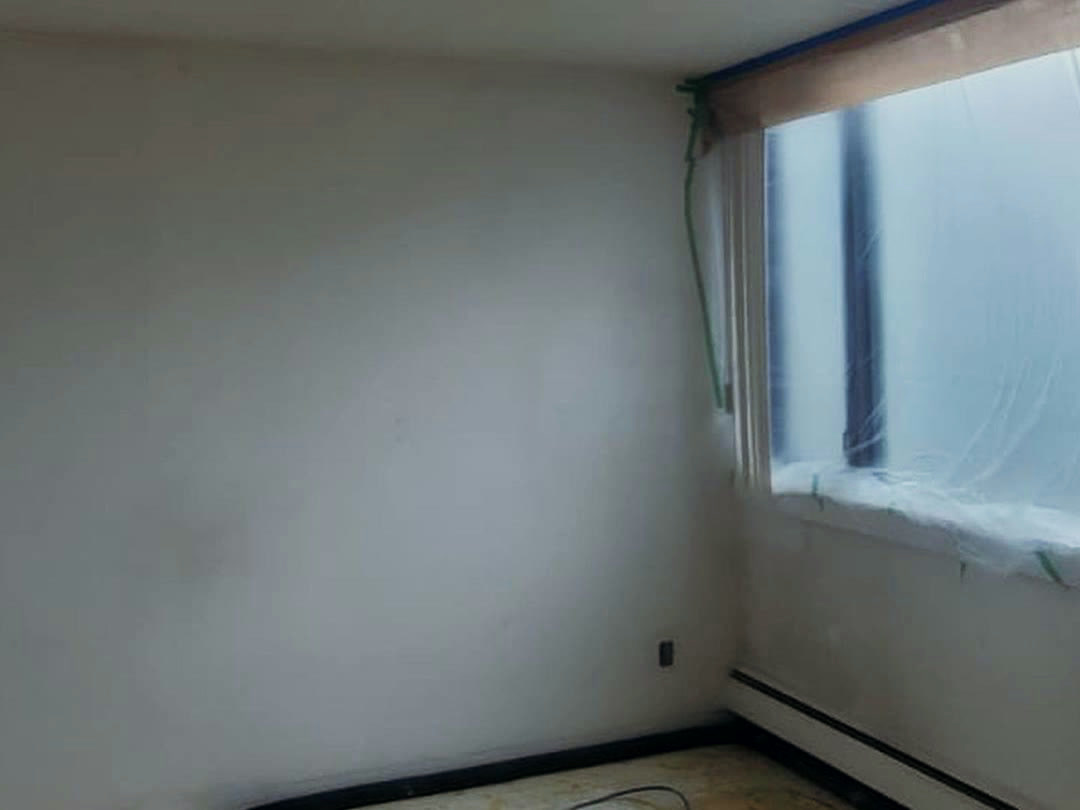 A bedroom masked off and prepared for spraying, with the window sheeted in plastic and the floor stripped back.