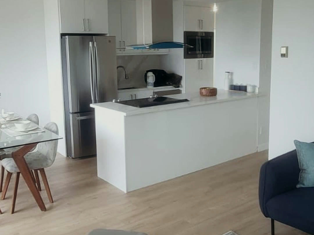 The completed kitchen, opened to the living area with a white island, induction cooktop, chimney hood and integrated appliances.
