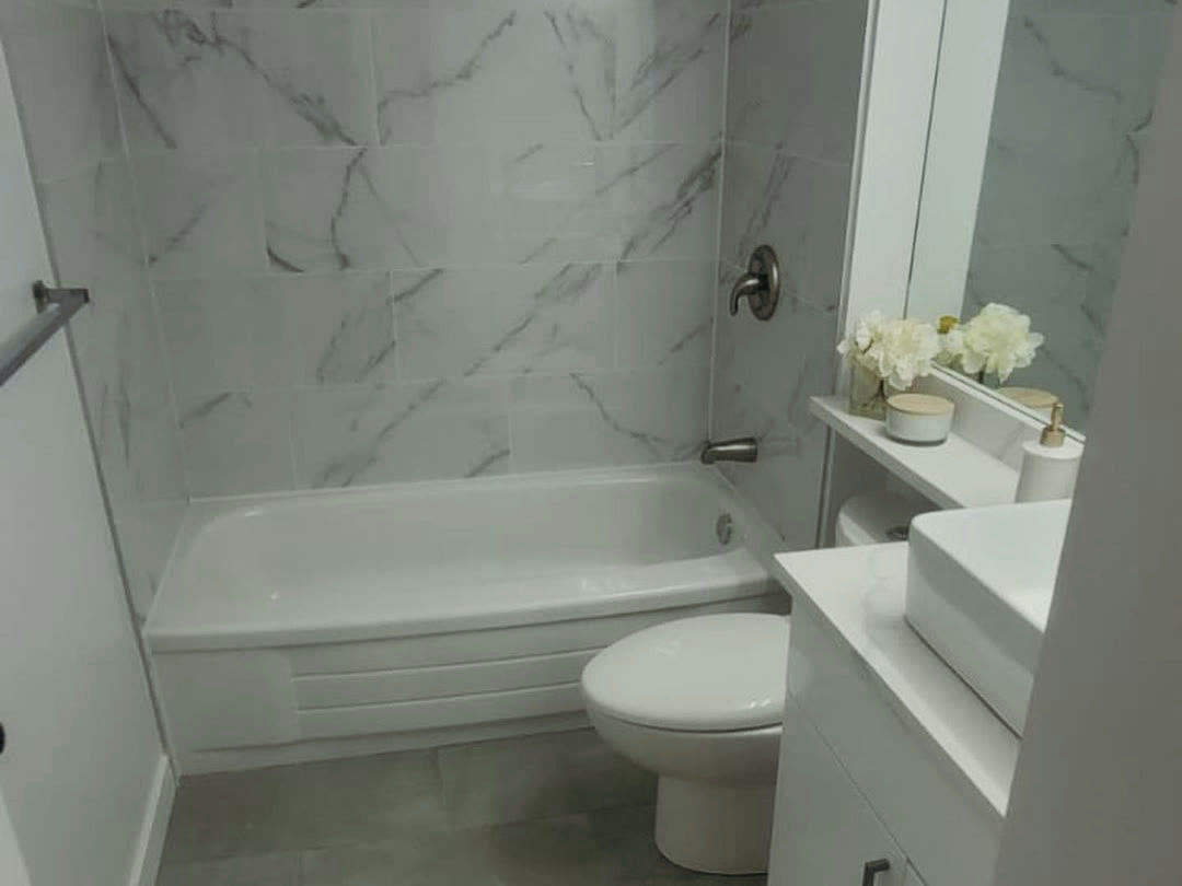 The completed bathroom, with a marble-look tiled tub surround, large-format grey floor tile and a new vanity.